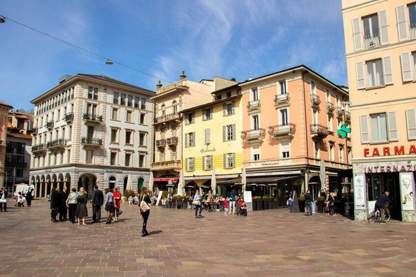 A bustling square with historic buildings, a pharmacy, and people walking. 2