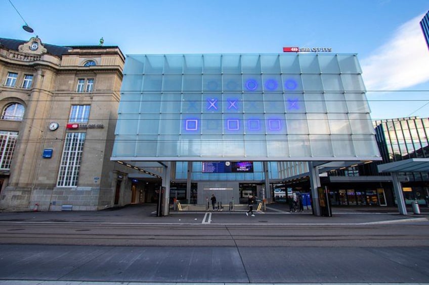 A modern building with a glass facade and a sign with blue squares and crosses. 2
