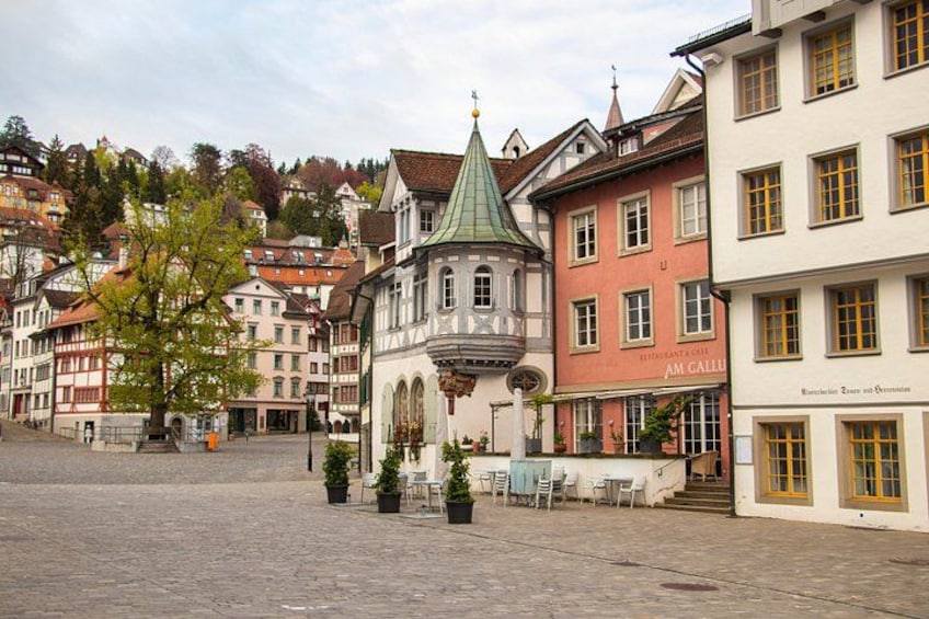 A cobblestone square with historic buildings, a church with a green roof, and outdoor seating. 3