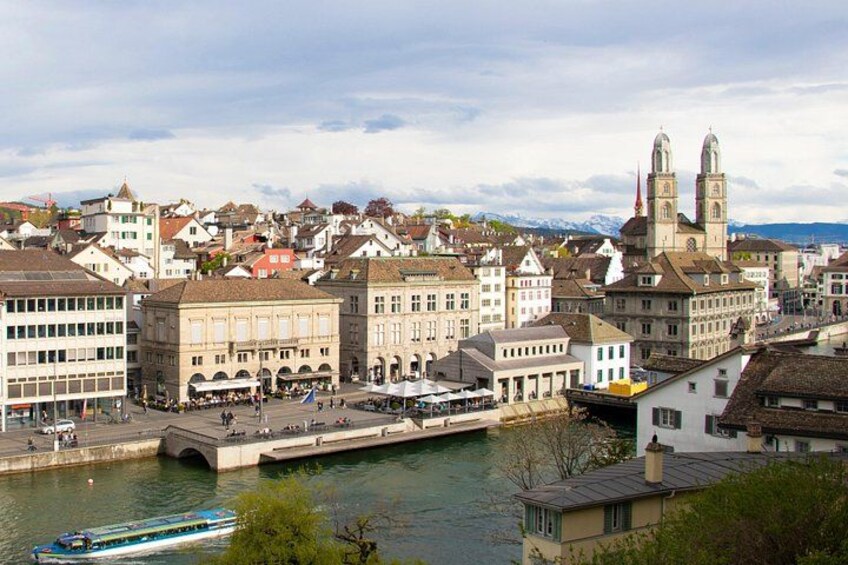 A riverside town with historic buildings, a prominent church with two towers, and a bridge over the water. 1