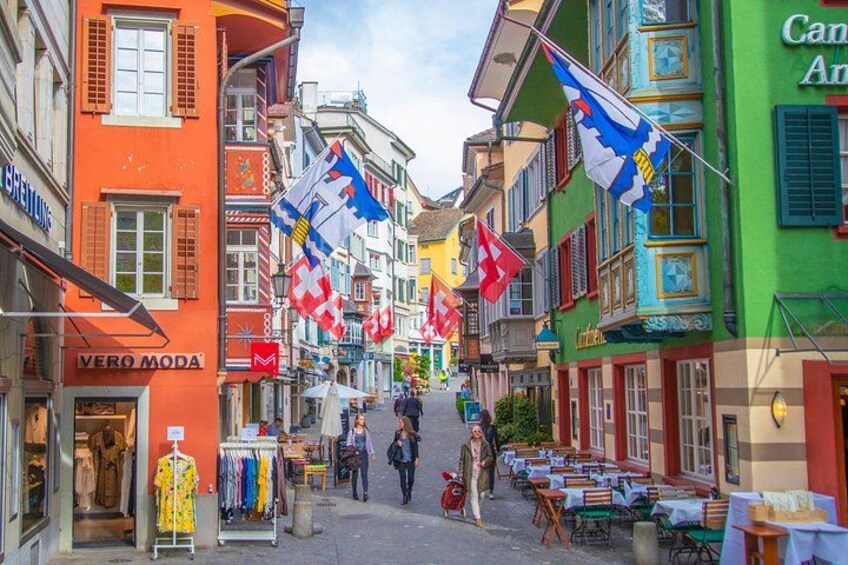 A street with colorful buildings, flags, and outdoor seating. 5