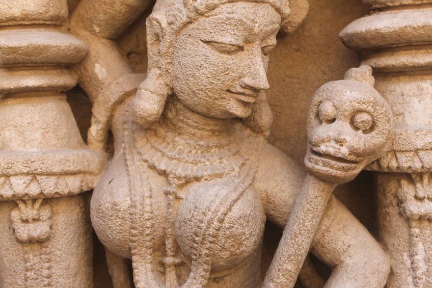 Une sculpture en pierre représentant une divinité avec un crâne, placée devant un décor en pierre sculptée. 1