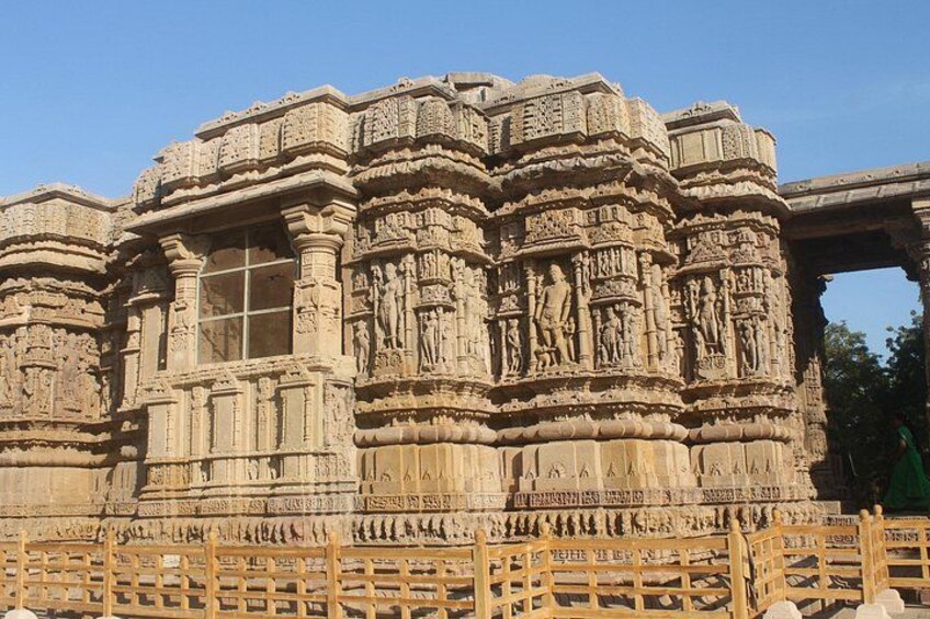 A detailed stone temple with intricate carvings and a wooden fence in the foreground. 1