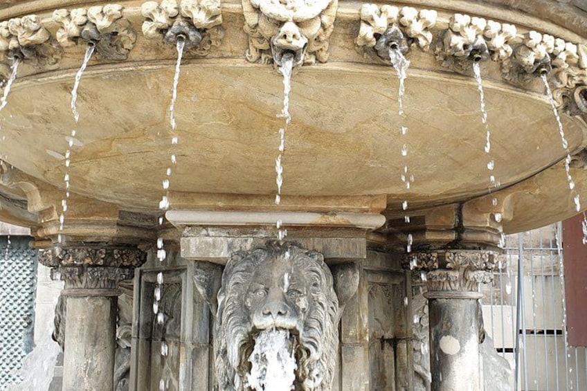 A stone fountain with water flowing from multiple spouts, surrounded by ornate carvings and columns. 2