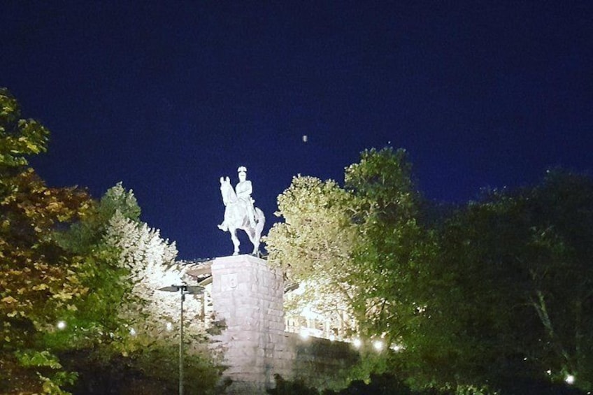 A statue on a pedestal at night, surrounded by trees and illuminated by street lamps. 2