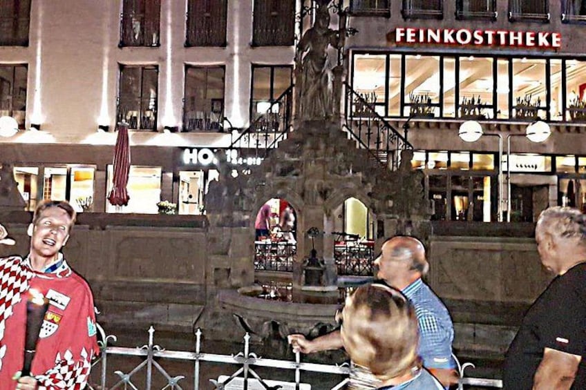 A fountain with a statue, a building with a sign reading 'FEINKOSTTHEKE,' and a person in a red jacket. 3