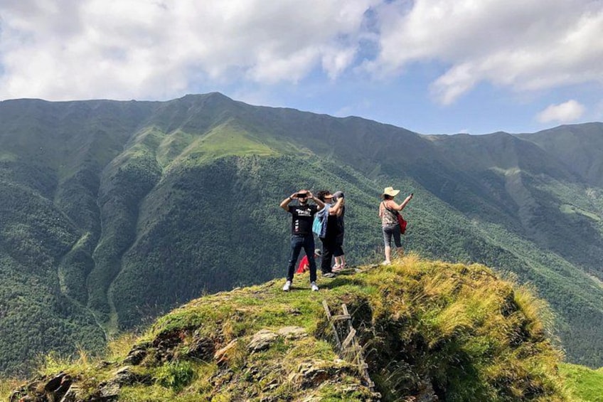 A group of people standing on a grassy hill overlooking a mountainous landscape. 2