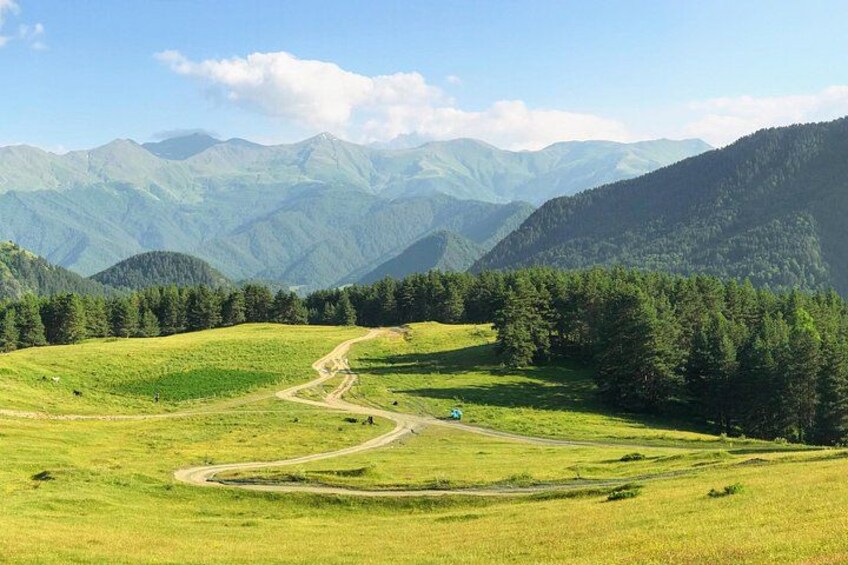 A winding road through a green valley with mountains in the background. 4