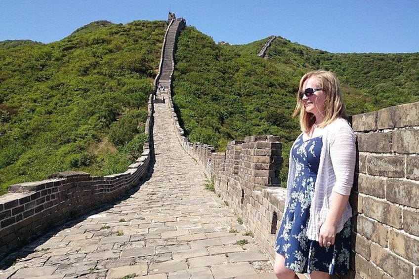A person standing on a stone pathway with a brick wall on one side and a green hill in the background. 4