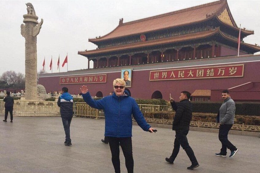 A person in a blue jacket with arms raised, a traditional Chinese building with red flags, and a stone monument in the foreground. 1