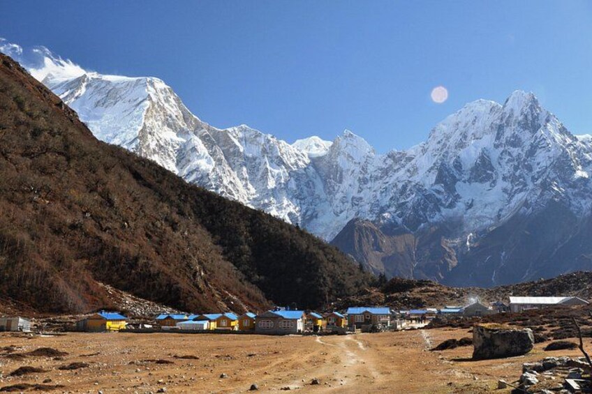 A mountainous landscape with snow-capped peaks, a clear sky, and a small settlement with buildings. 1