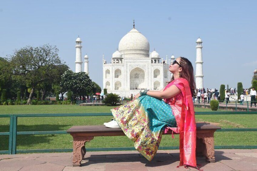 A woman sitting on a bench with the Taj Mahal in the background. 3