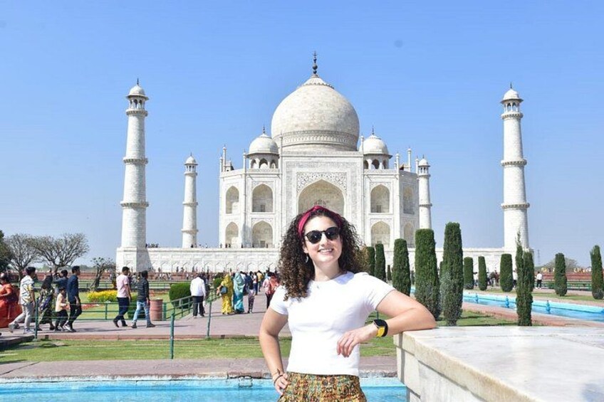 Een persoon staat voor de Taj Mahal, met vier minaretten en de omliggende tuin. 1