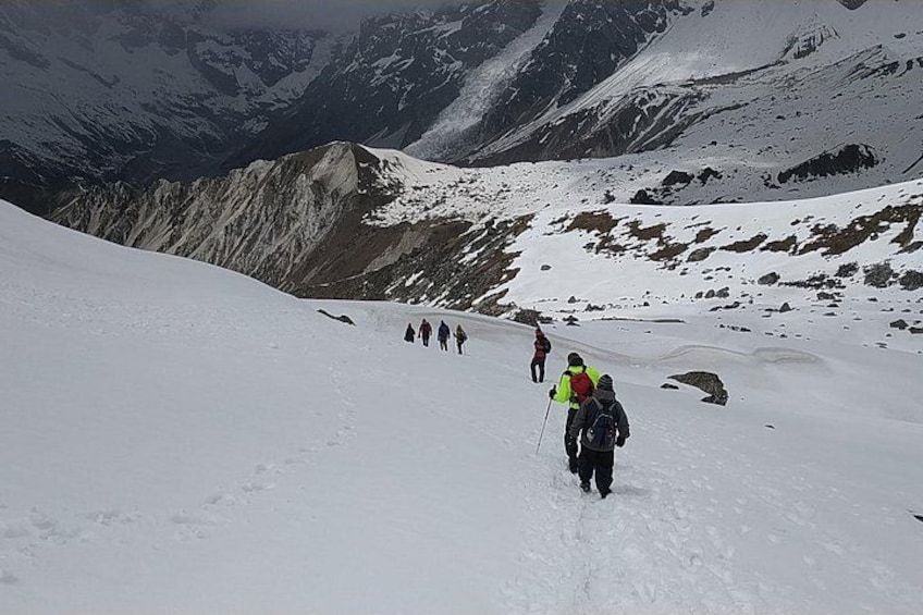 A group of hikers on a snowy mountain trail with rocky terrain and snow-covered peaks in the background. 1
