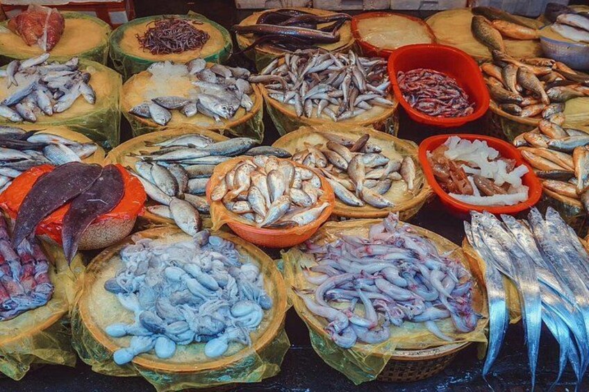 Verschiedene Fische werden in Körben und Schalen auf einem Markt präsentiert. 1