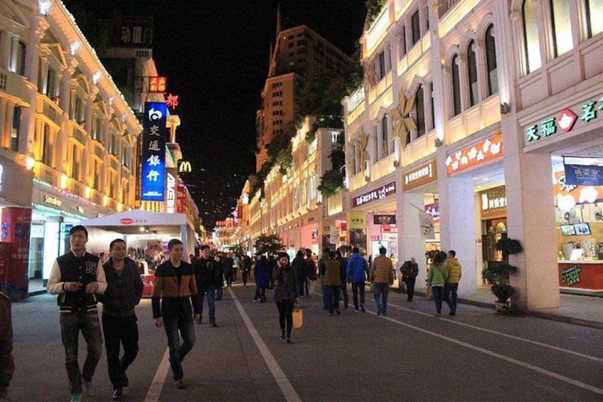 Eine belebte Stadtstraße bei Nacht mit beleuchteten Schaufenstern und Fußgängern. 5
