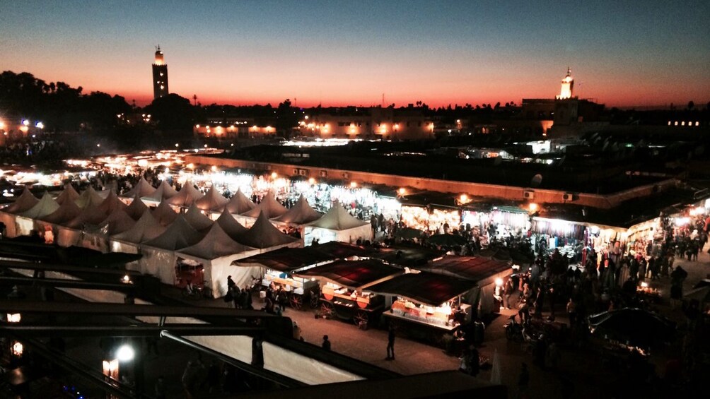 A nighttime market with tents and stalls, a prominent tower, and a mosque with a minaret. 4
