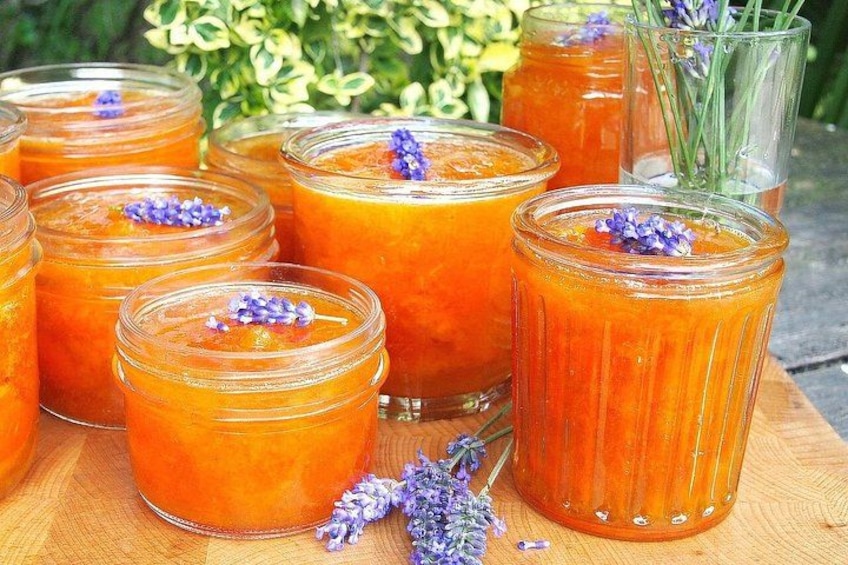 A collection of orange drinks in glass jars and a glass, with purple flowers as garnish. 1
