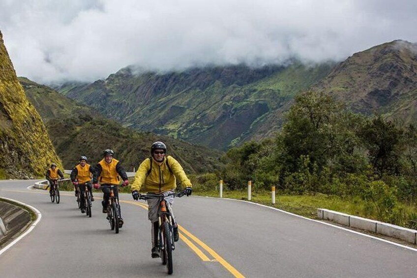 A group of cyclists on a winding mountain road surrounded by lush greenery and hills. 1