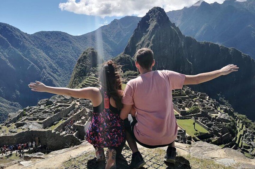 A couple standing with arms outstretched at Machu Picchu, overlooking the ruins and mountains. 4
