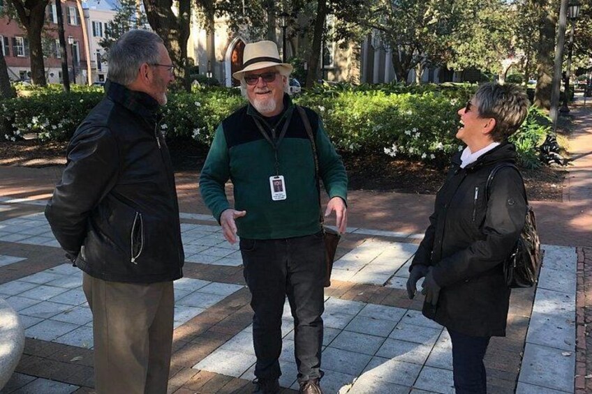 Tres personas conversando en un sendero adoquinado, con árboles y edificios al fondo. 1