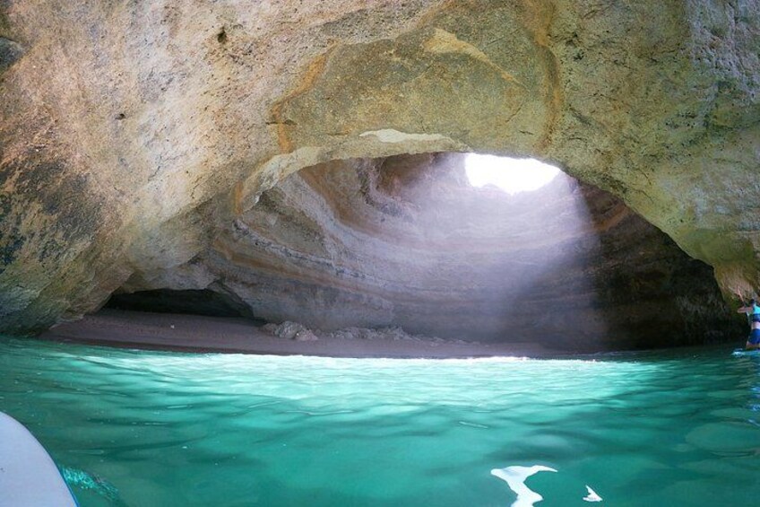 A natural rock formation with a cave entrance, clear turquoise water, and a boat. 5
