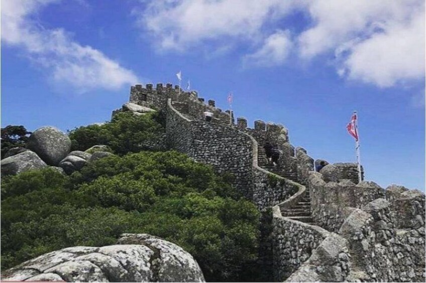 A stone wall with flags, surrounded by greenery and rocks. 1