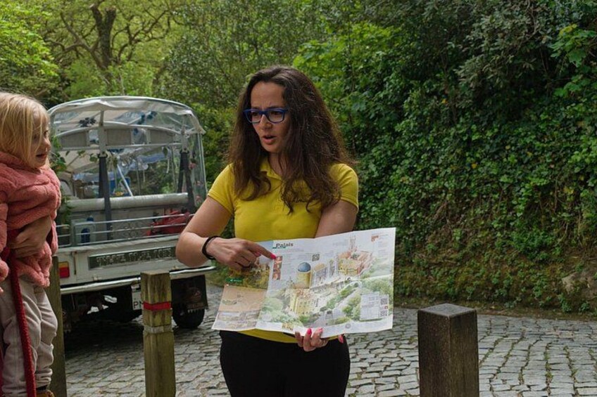 A person holding a map, standing next to a vehicle on a cobblestone path in a wooded area. 3