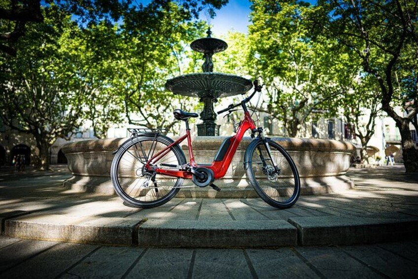 A red electric bicycle parked in front of a fountain in a park. 4
