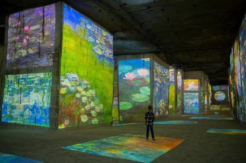 A person standing in a room with large, colorful light projections on the walls and floor. 1