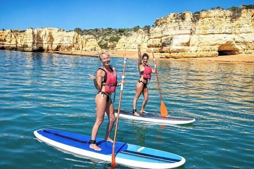 Two people paddleboarding on calm waters with rocky cliffs in the background. 5