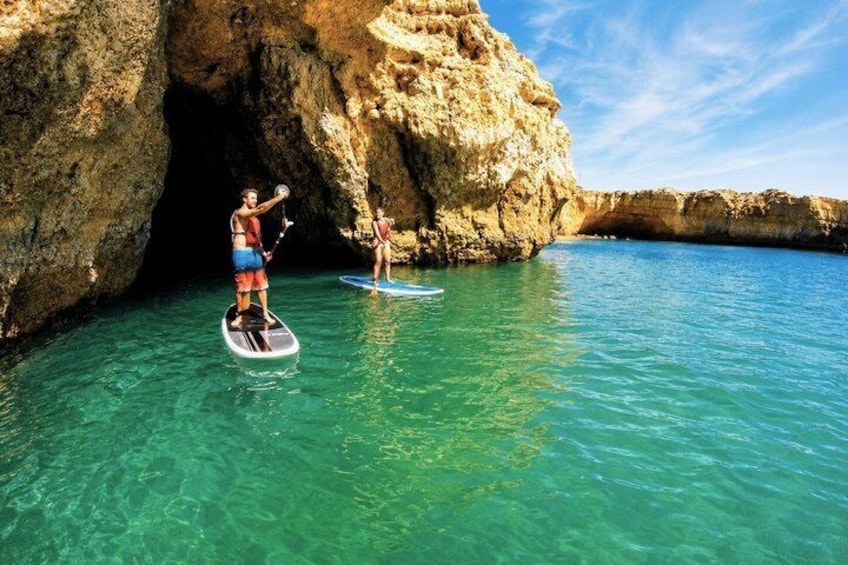 Two people paddleboarding near a rocky coastline. 1