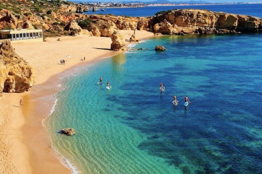 A coastal beach with clear water, rocky cliffs, and people swimming. 4