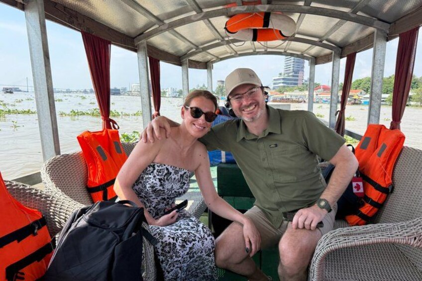 Two people on a boat with life jackets, a cityscape in the background, and water in the foreground. 4