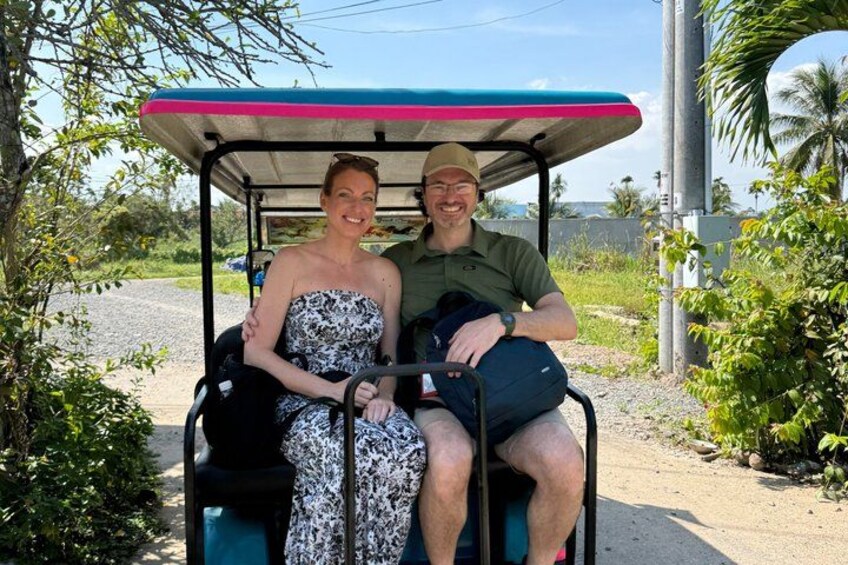 A couple in a golf cart on a road with greenery and a clear sky. 2
