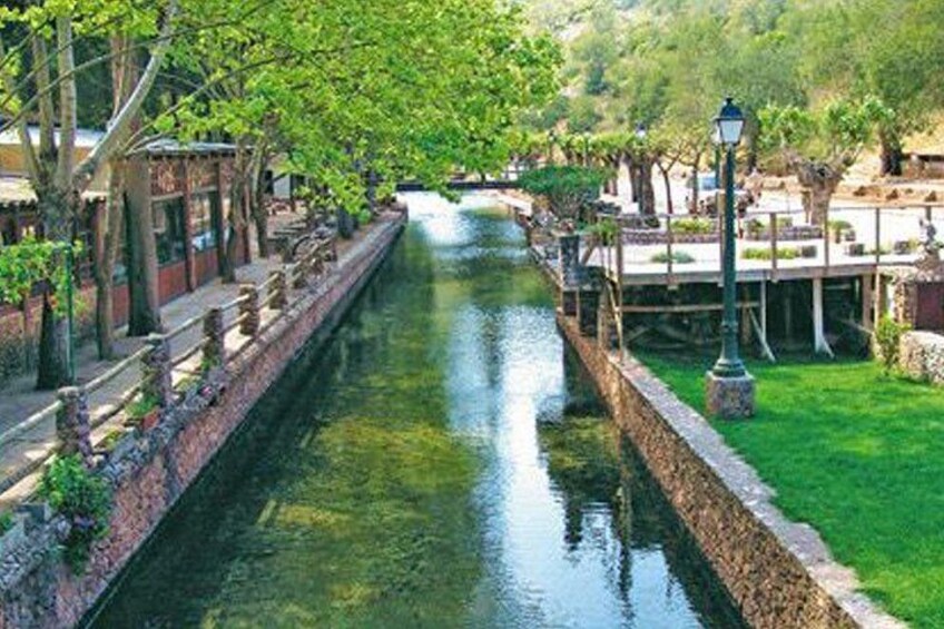 A canal with buildings on either side, a grassy area, and trees. 2