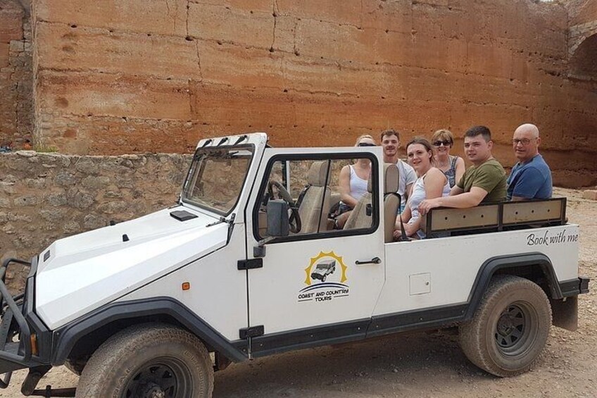 A white safari vehicle with passengers, a rocky landscape, and a large rock formation in the background. 5