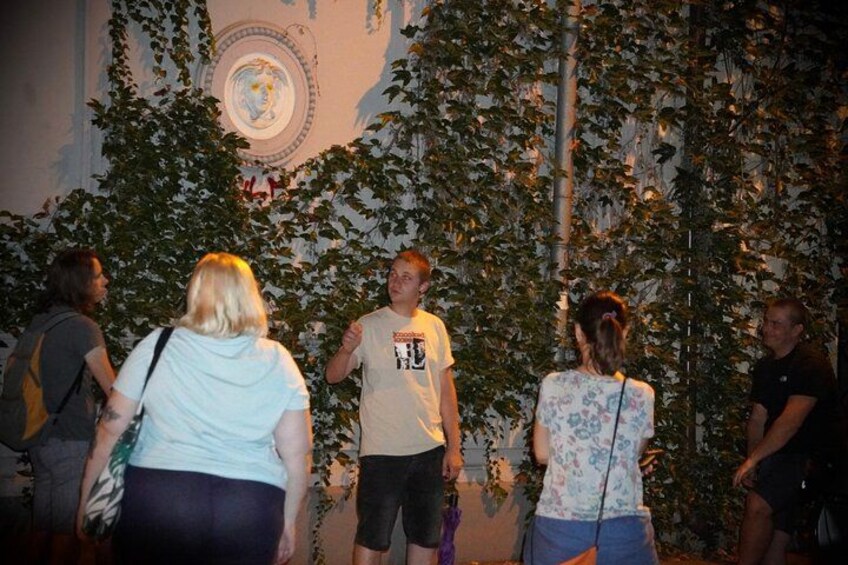 A group of people standing in front of a wall with a circular design and climbing plants. 1