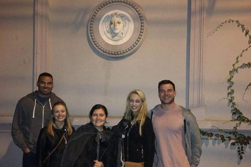 En grupp människor som står inomhus framför en dekorativ vägg, med en växt i bakgrunden. 2