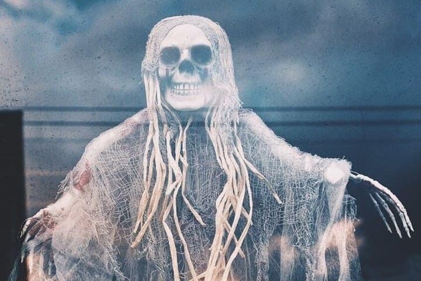 A figure in a skeletal costume with long, white, rope-like hair, standing against a cloudy sky. 2
