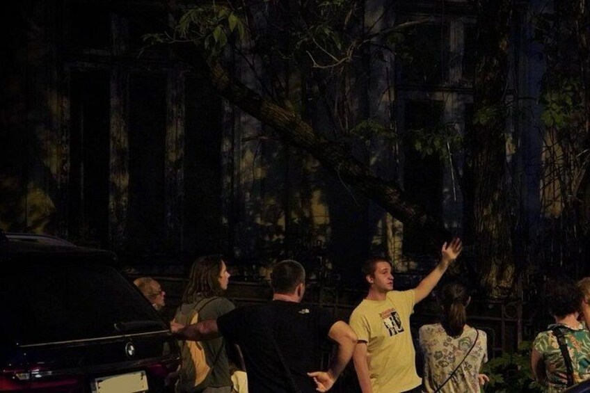 A group of people outdoors at night, with trees and a building in the background. 5