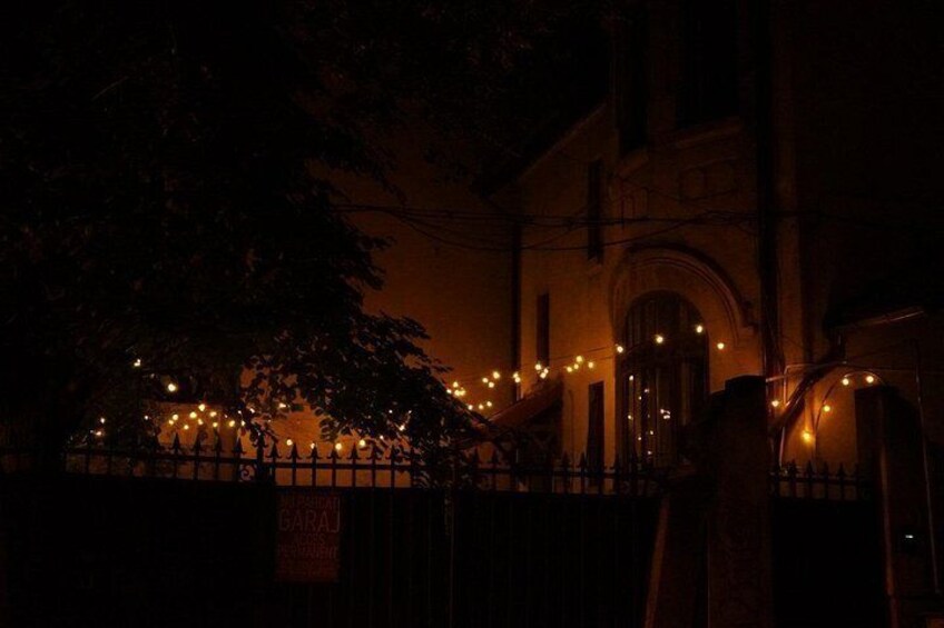 A building with a dark facade, a tree in the foreground, and a fence with lights. 2