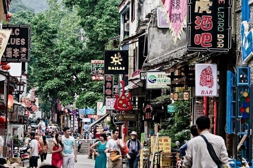 Un marché de rue animé, avec de nombreux commerces et enseignes, notamment une enseigne « Railas » et une enseigne « Bar ». 1