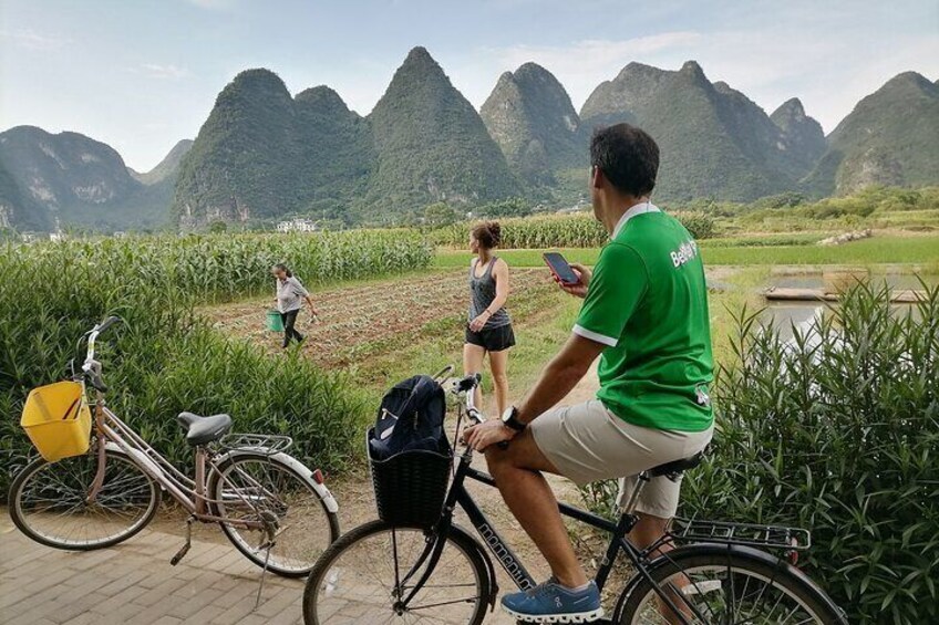 Een man op een fiets, een vrouw die loopt, en een andere vrouw die staat in een veld met bergen op de achtergrond. 4