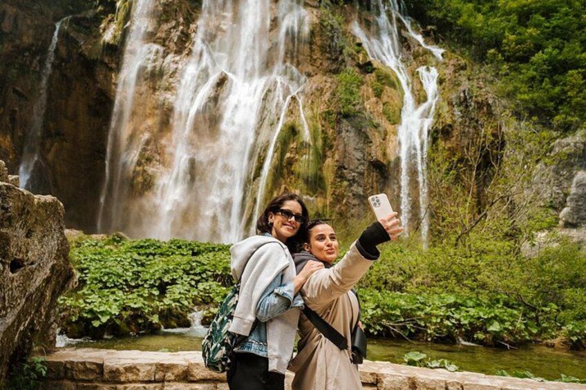Two smiling women pose in front of the stunning waterfalls at Plitvice Lakes National Park, surrounded by lush greenery and crystal-clear waters, a perfect snapshot of Croatia’s natural beauty. 5