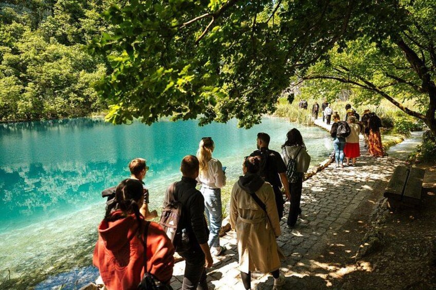 Tourists stroll along the wooden paths beside a clear lake at Plitvice Lakes National Park, surrounded by serene nature and vibrant greenery. 3