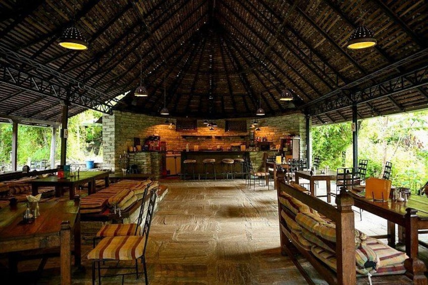 Een eethoek met houten tafels en banken, een bakstenen muur en een rieten dak. 3