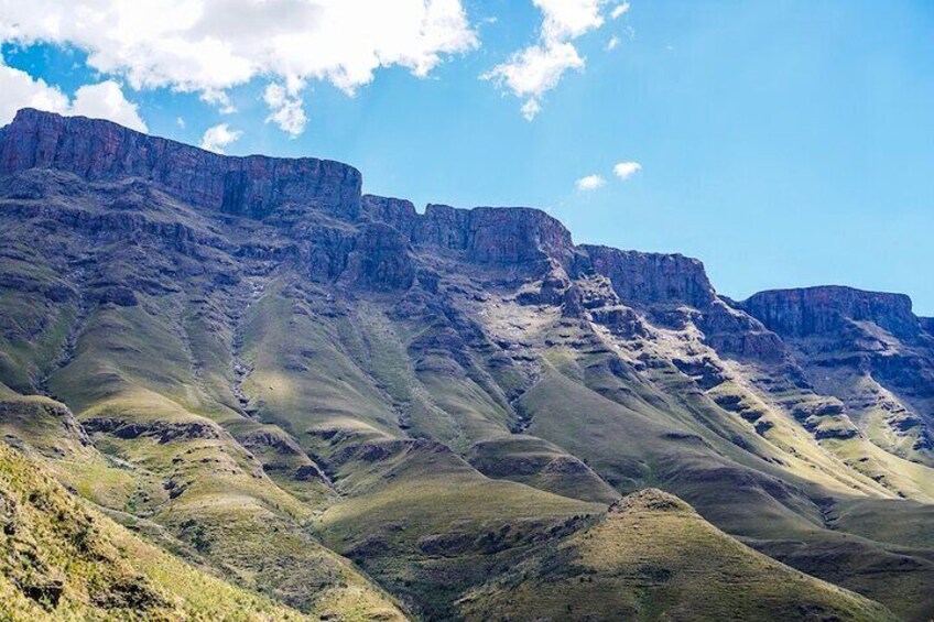 A mountainous landscape with rugged cliffs and rolling hills under a clear sky. 1