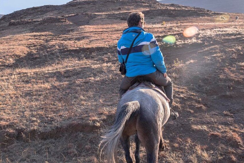 A person riding a horse on a dry, grassy hillside during sunset. 1