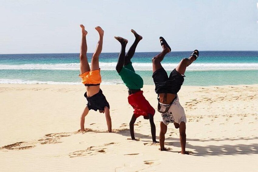 Tres personas haciendo parada de manos en una playa arenosa, con el océano al fondo. 2